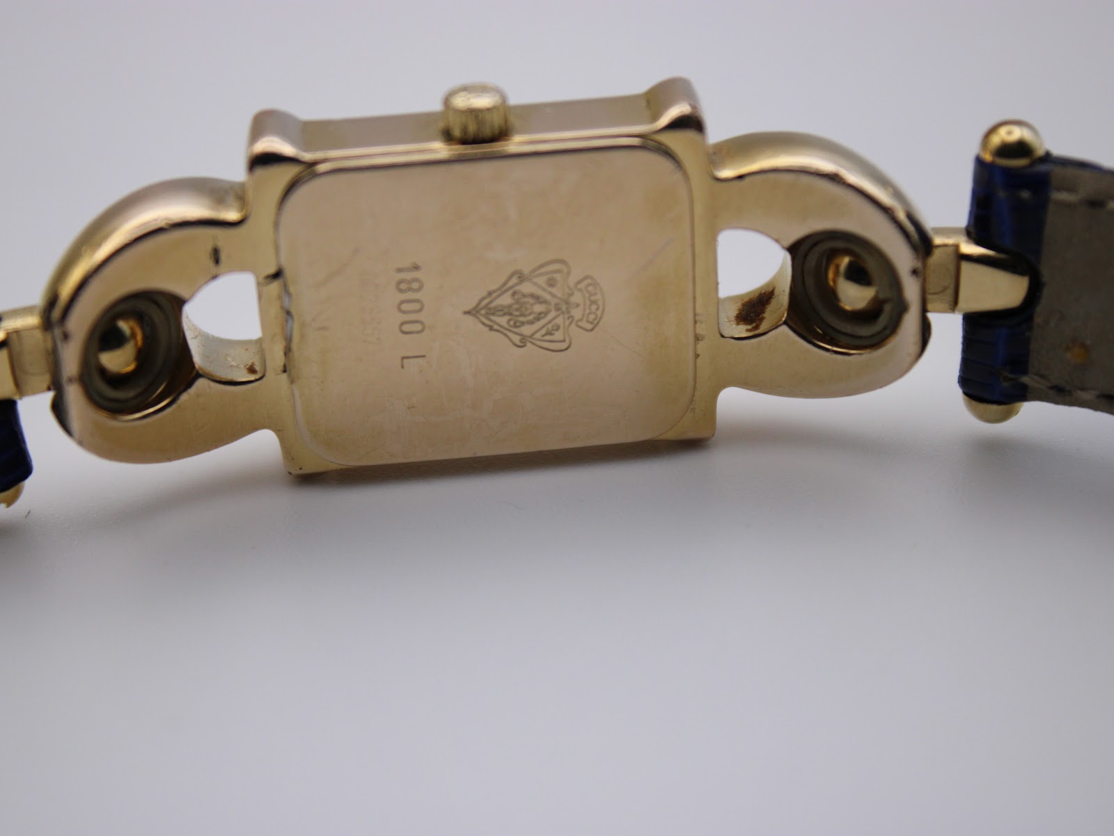 Close-up of the gold plated rectangular case back showing '1800 L' engraving and the Gucci logo.