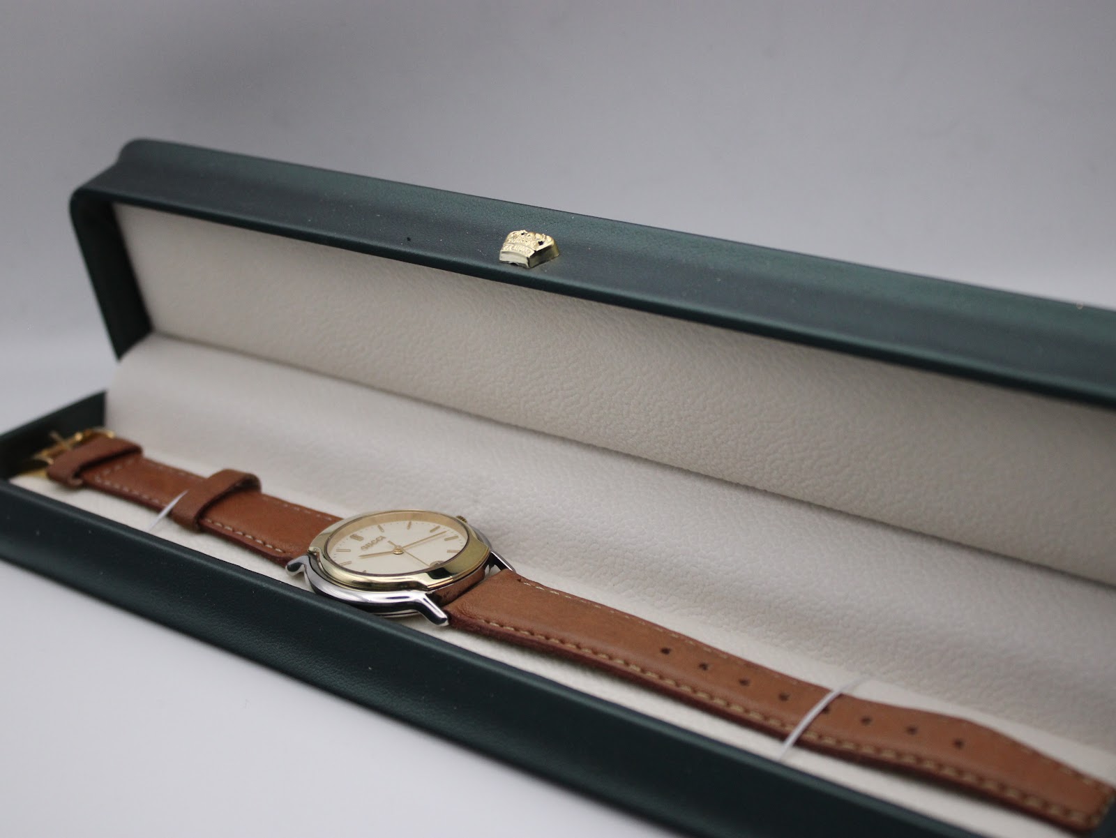 Gucci watch with brown leather strap displayed in a green presentation box.