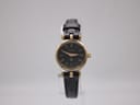 Front view of Gucci 2000L gold-tone watch with black dial and leather strap on a display stand.