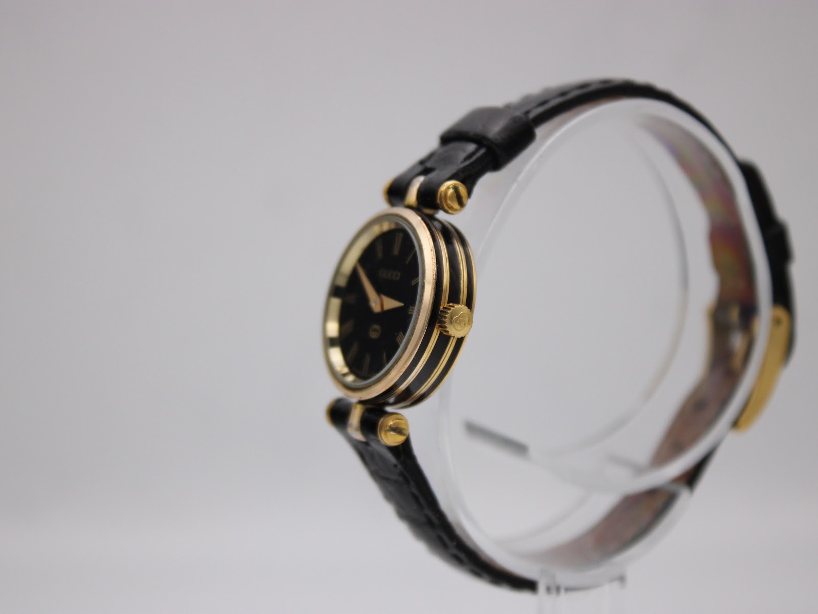 Right side view of the Gucci 2000L watch, showing gold-tone case, original crown, and black leather strap on a stand.