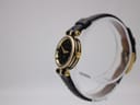 Right side view of the Gucci 2000L watch, showing gold-tone case, original crown, and black leather strap on a stand.