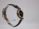 Left side view of the Gucci 2000L watch, showing gold-tone case and black leather strap on a stand.