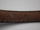 Close-up of the embossed 'GUCCI' logo on the brown underside of the black leather watch strap.