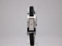 Front view of the Gucci 3900L watch on a clear stand, showing its rectangular stainless steel case, white dial with Gucci logo, and black leather strap.