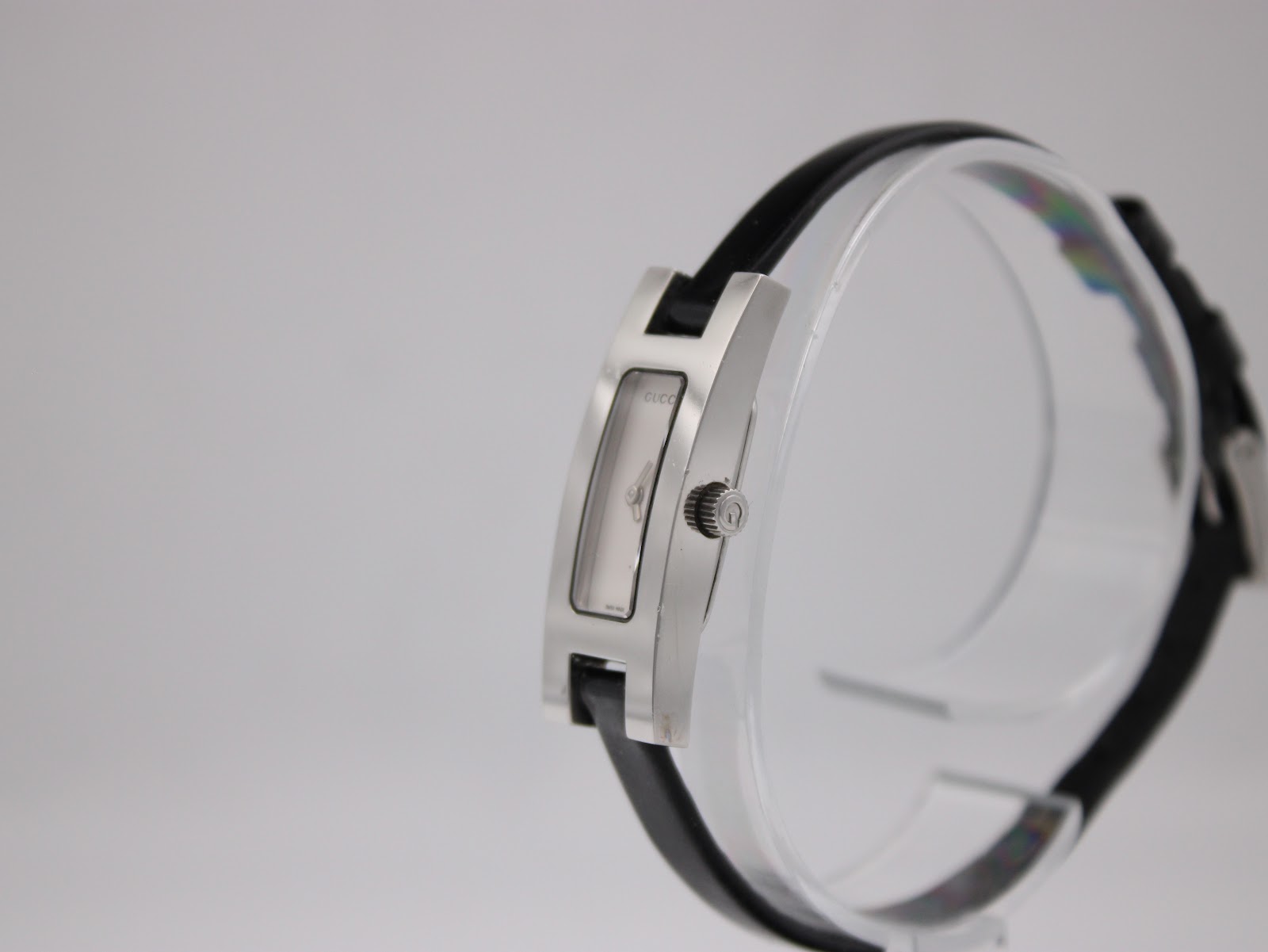 Side-angled view of the Gucci 3900L watch on a clear stand, highlighting the slim profile of the stainless steel case and the original signed crown.