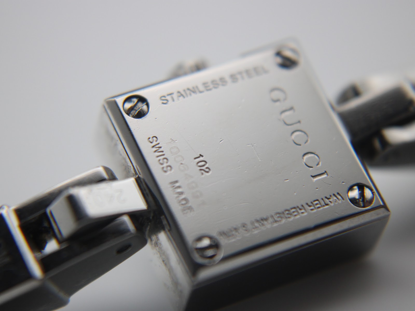 Close-up of the watch case back showing "Stainless Steel", "Gucci", "Swiss Made", "102", "10064991" serial, and "Water Resistant 3ATM" engravings.