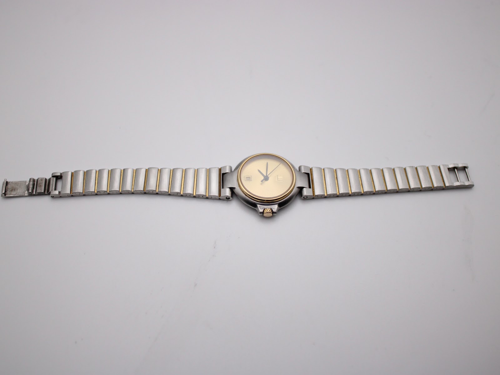 Dunhill watch with two-tone bracelet laid flat, showing the gold sunburst dial.