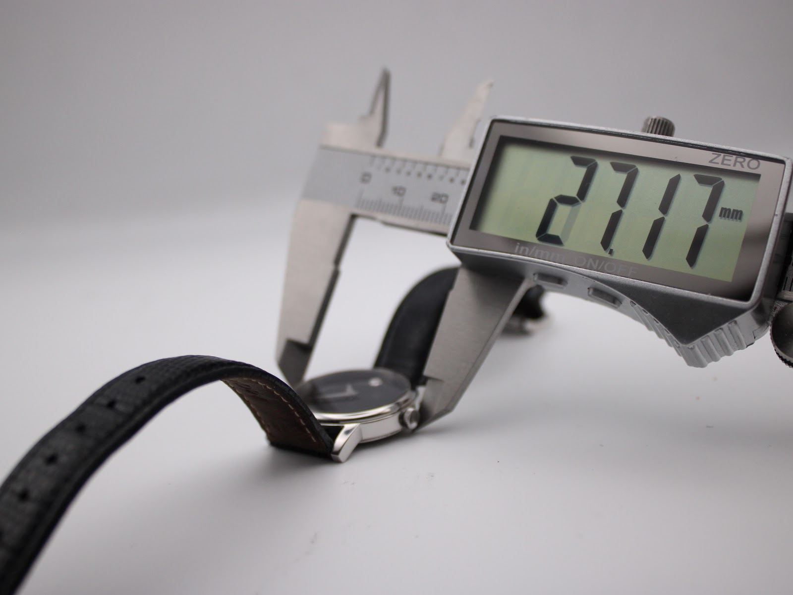Digital caliper measuring the case diameter of the watch, displaying the precise measurement of 27.17 mm on its screen.