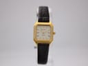 Front view of the gold-tone Bulova G77A watch on a clear stand, showing its cream dial and dark brown leather strap.