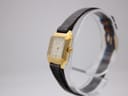 Angled side view of the Bulova watch on a stand, highlighting the gold-tone case and crown, with the dark brown leather strap.