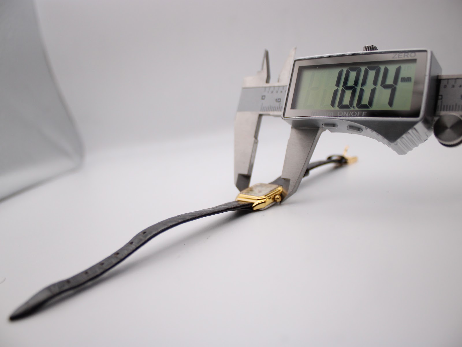 Side view of the watch being measured by a digital caliper, displaying a precise case diameter of 18.04 mm.