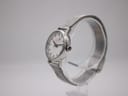 Side angled view of Mondaine watch showing stainless steel case and mesh bracelet on a display stand.