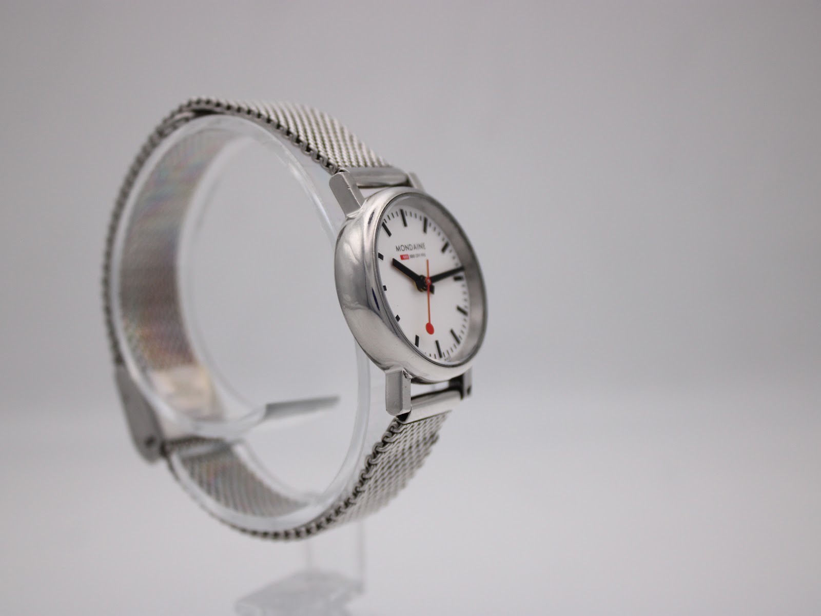 Angled side view of the watch on a display stand, highlighting the mesh bracelet.