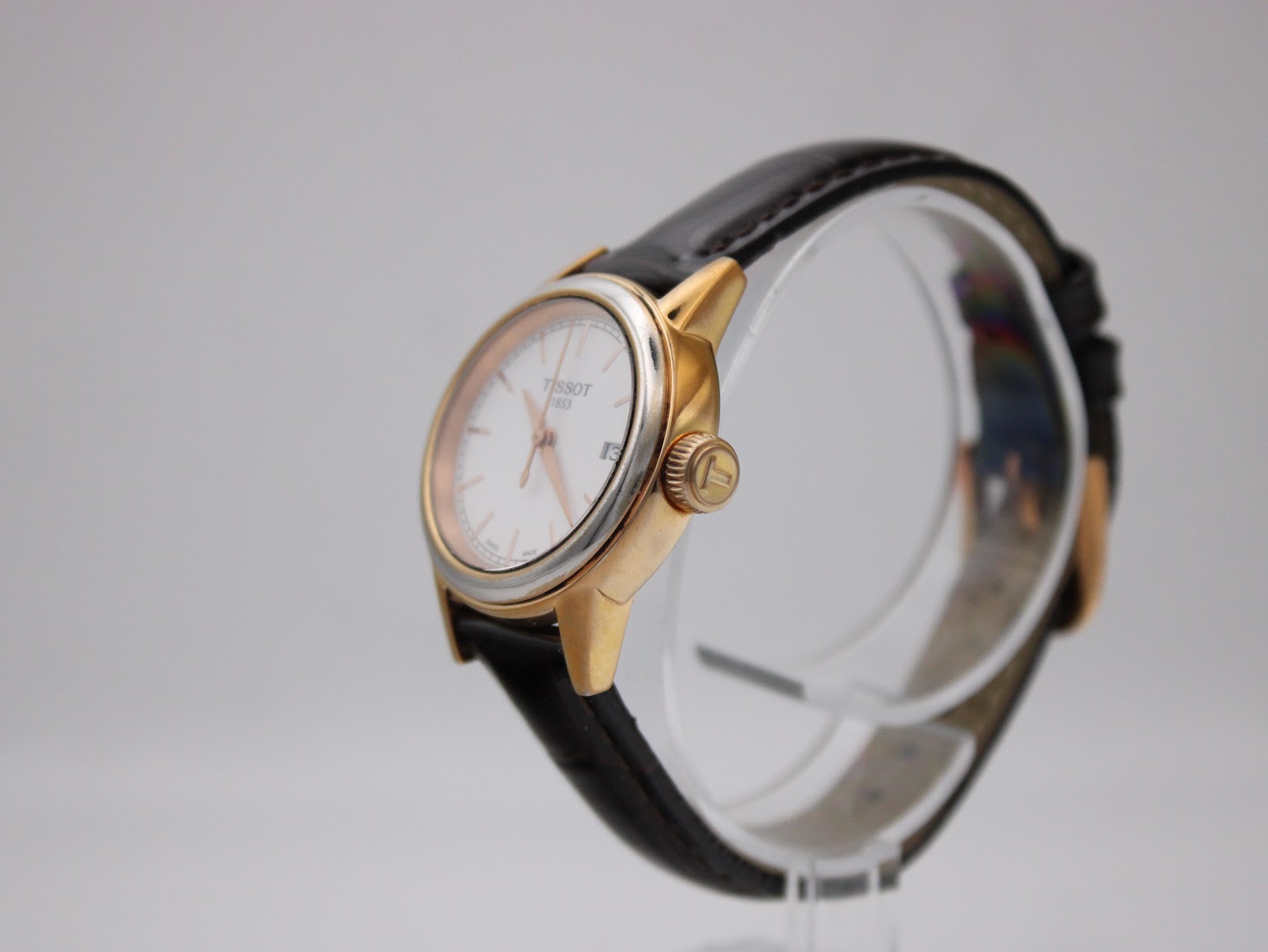 Angled side view of the Tissot watch on a display stand, showing the gold-tone case and signed Tissot crown.