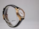 Opposite angled side view of the Tissot watch on a display stand, highlighting the gold-tone case and dark brown leather strap.