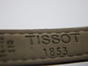 Close-up of the underside of the dark brown leather strap with "TISSOT 1853" embossed.