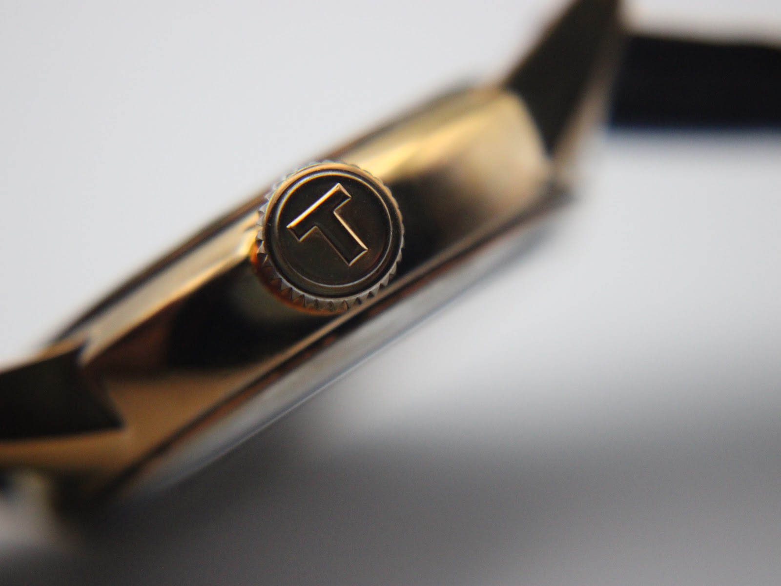 Macro shot of the gold-tone crown with the Tissot 'T' logo engraved on its end.