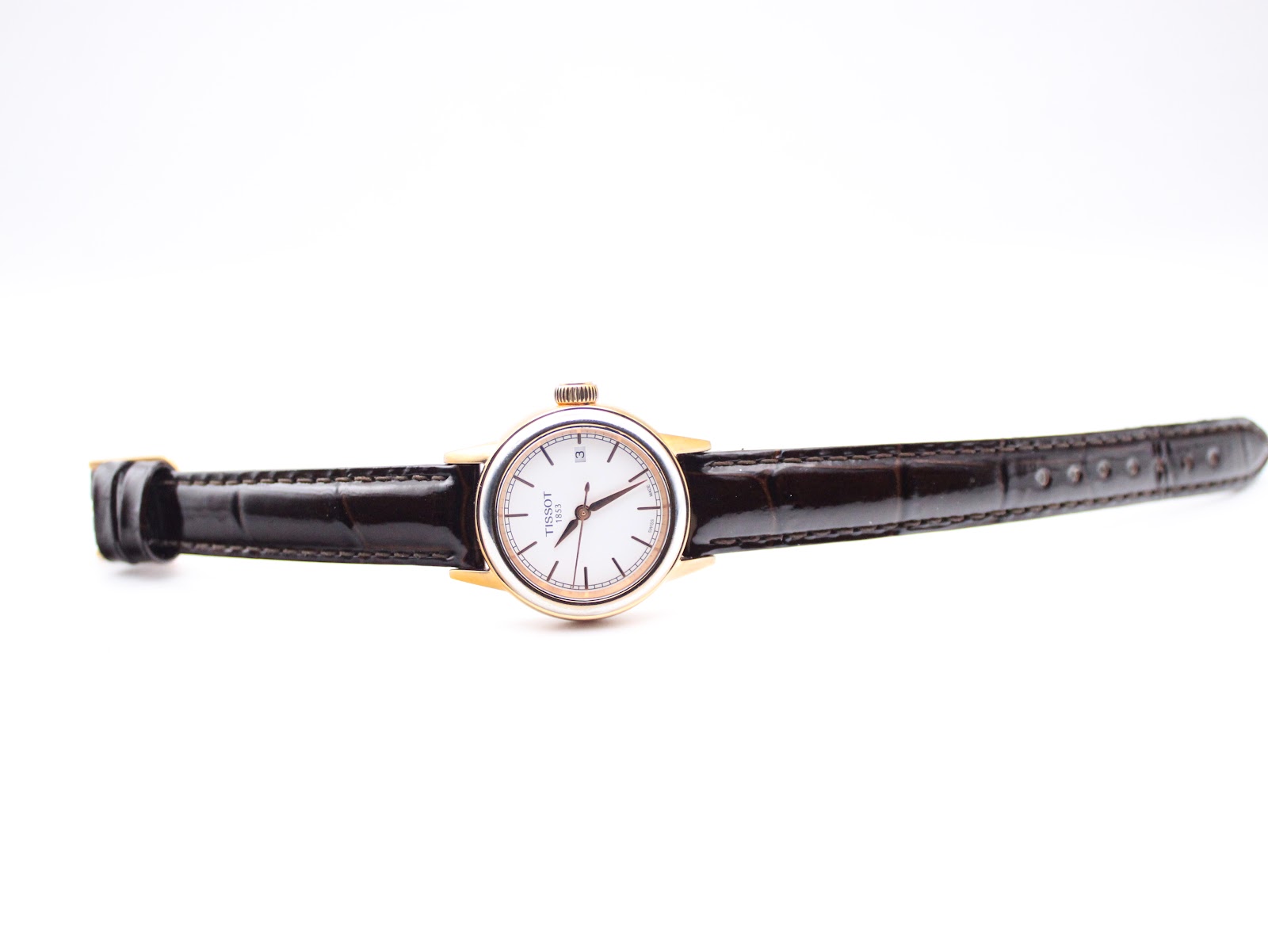 Full length view of the Tissot watch laid flat with the dark brown leather strap extended.