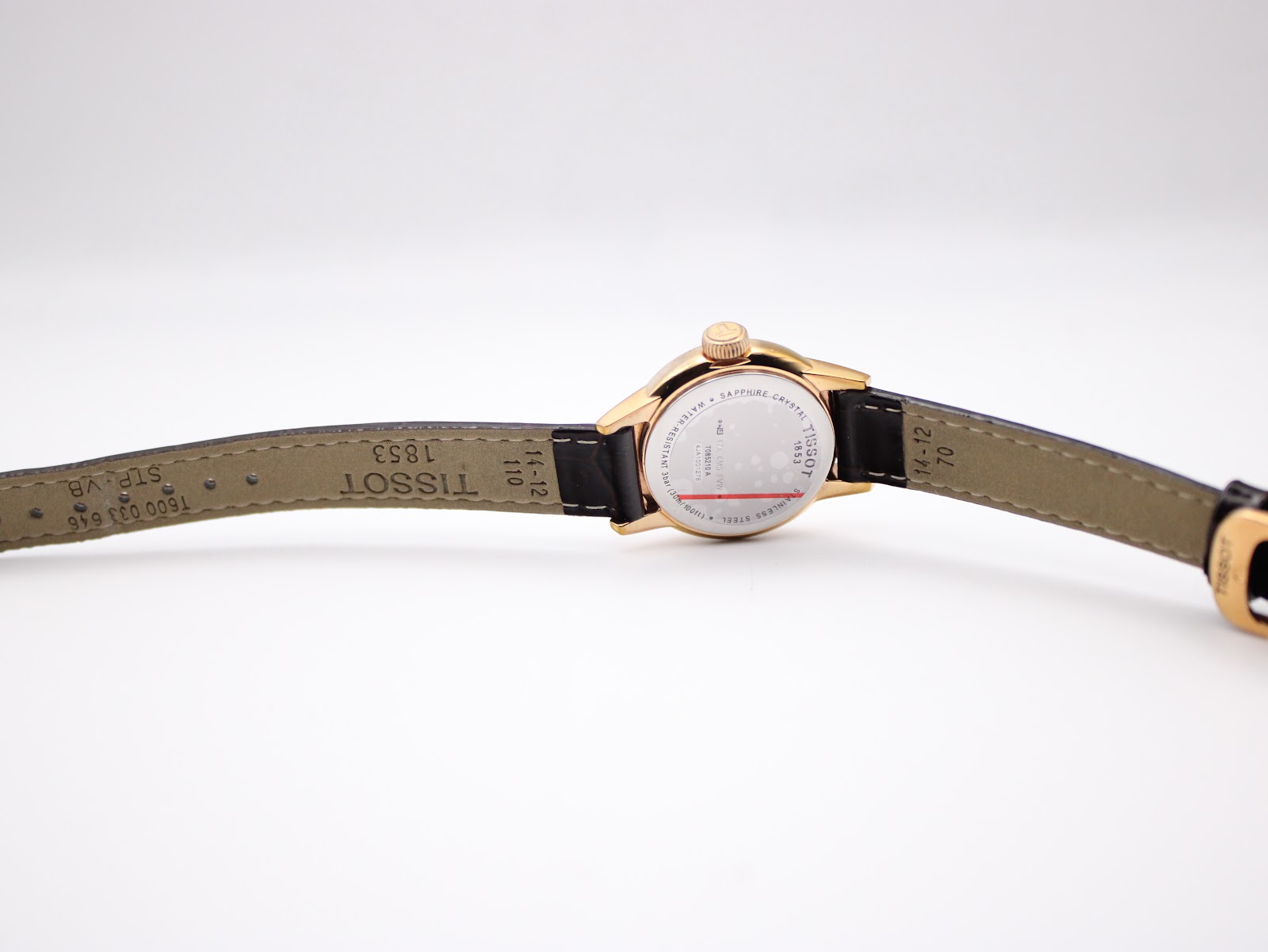 Underside view of the Tissot watch with the dark brown leather strap extended, showing strap markings and case back.