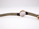Underside view of the Tissot watch with the dark brown leather strap extended, showing strap markings and case back.