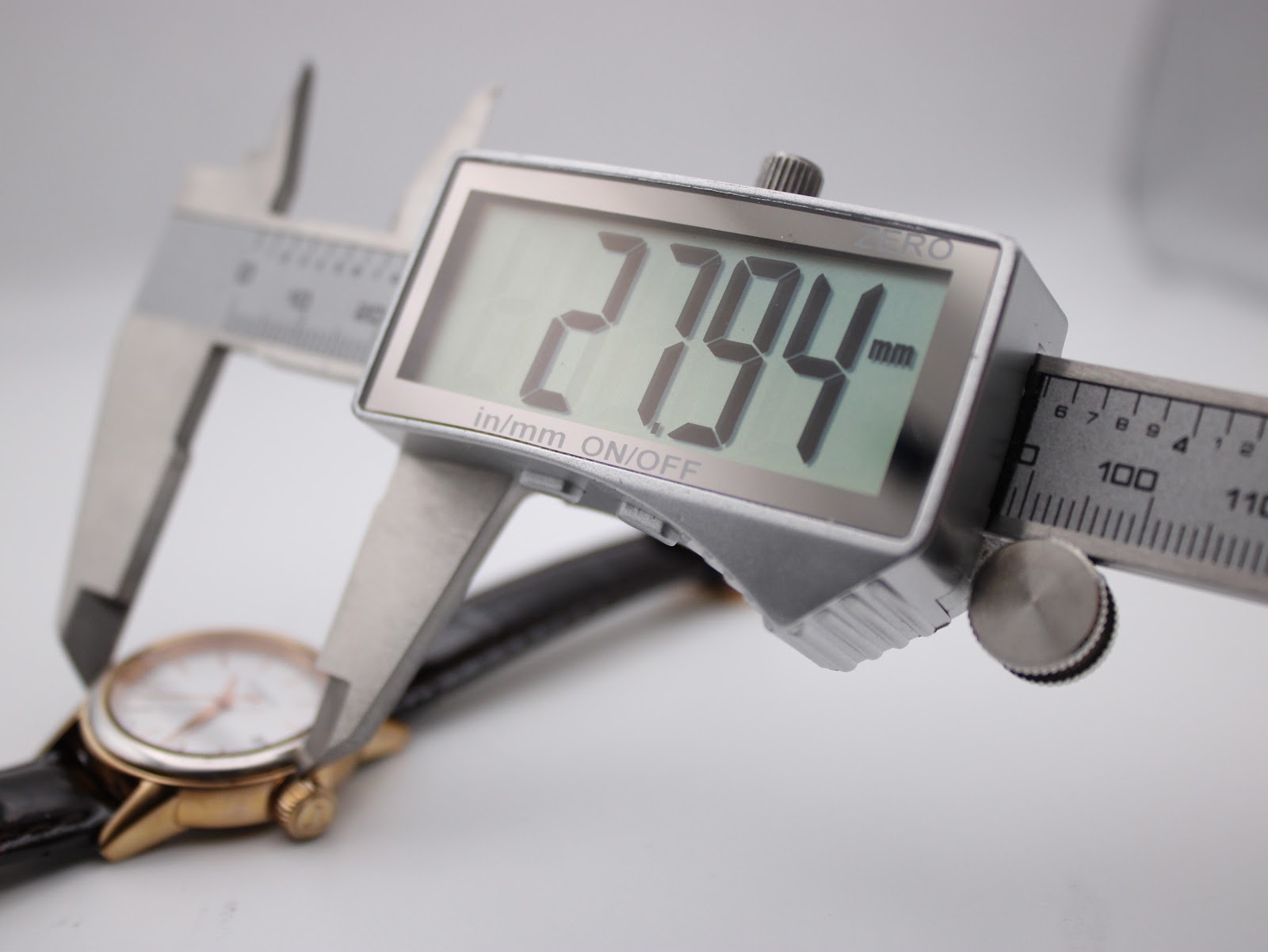 Digital caliper measuring the watch case diameter, displaying 27.94 mm.