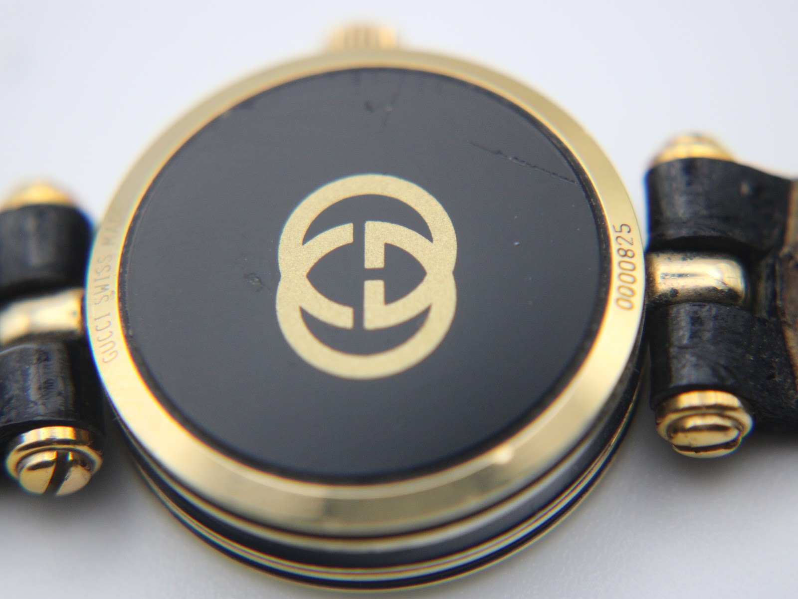 Close-up view of the black case back of the Gucci 2000L, with the gold-tone interlocking G logo and serial number 0000825 visible.