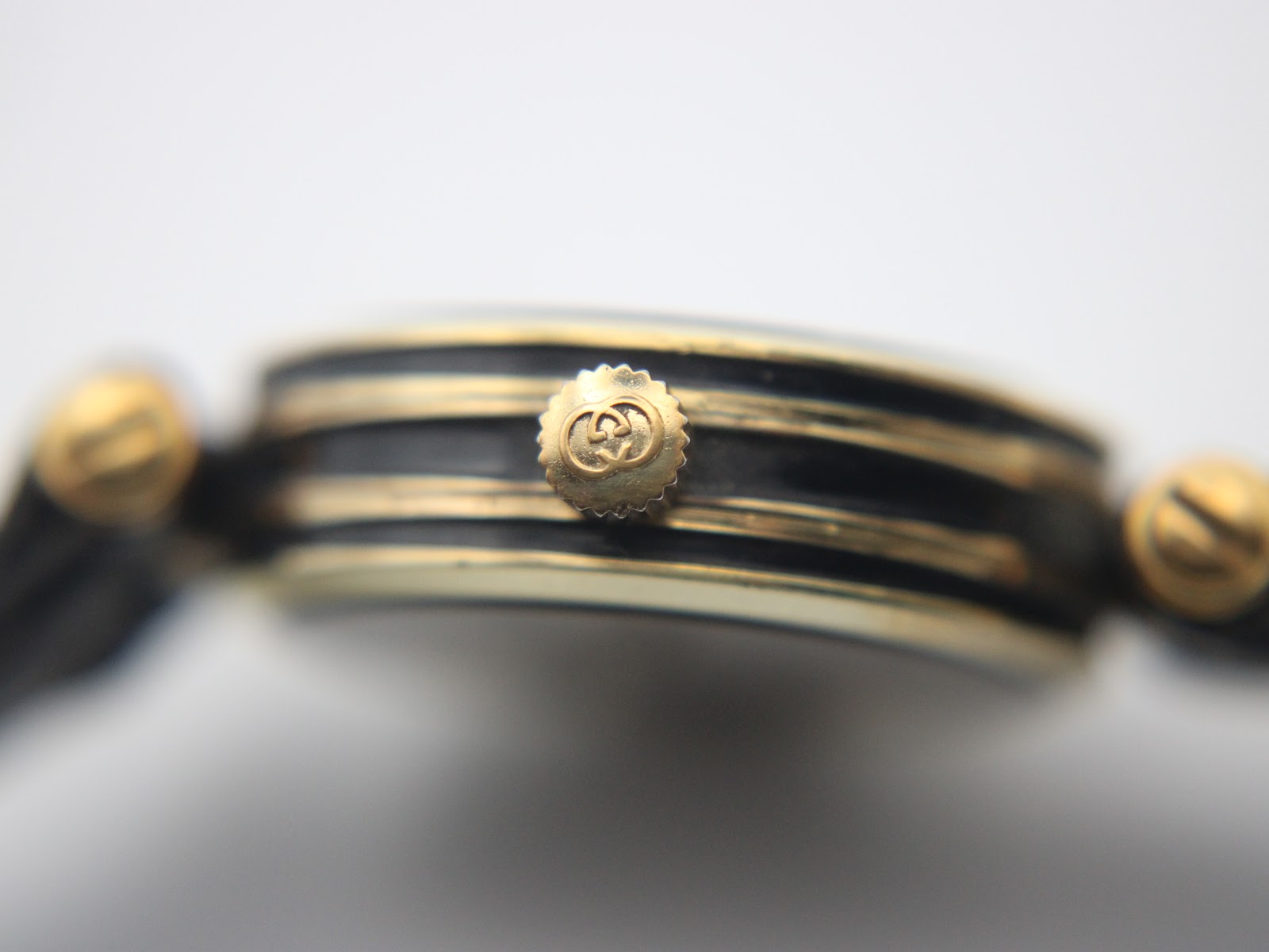 Detailed close-up of the gold-tone crown, clearly showing the embossed Gucci logo.