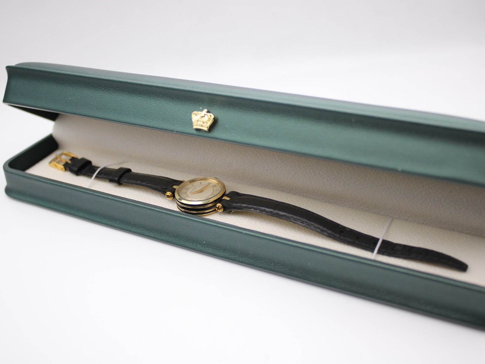 The Gucci 2000L watch presented in a green hinged display box with a crown motif, resting on a light-coloured interior.