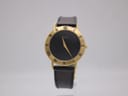 Front view of the Gucci 3000.2.M watch, featuring a black dial with gold roman numerals and gold-tone hands, on a clear display stand.