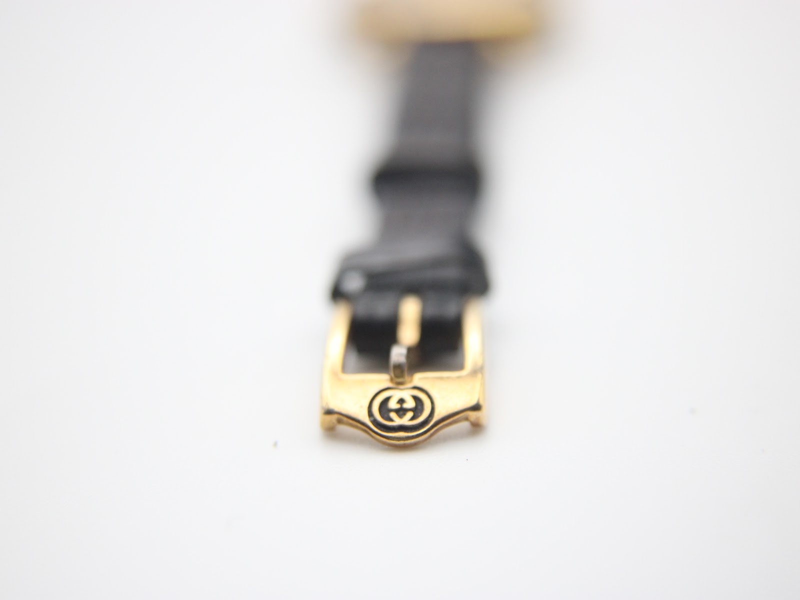 Close-up of the gold-plated buckle on the black leather strap, featuring the engraved Gucci logo.