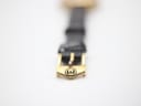 Close-up of the gold-plated buckle on the black leather strap, featuring the engraved Gucci logo.