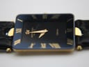 Close-up, slightly angled view of the black dial with gold hands and 'Raymond Weil Genève Othello' text
