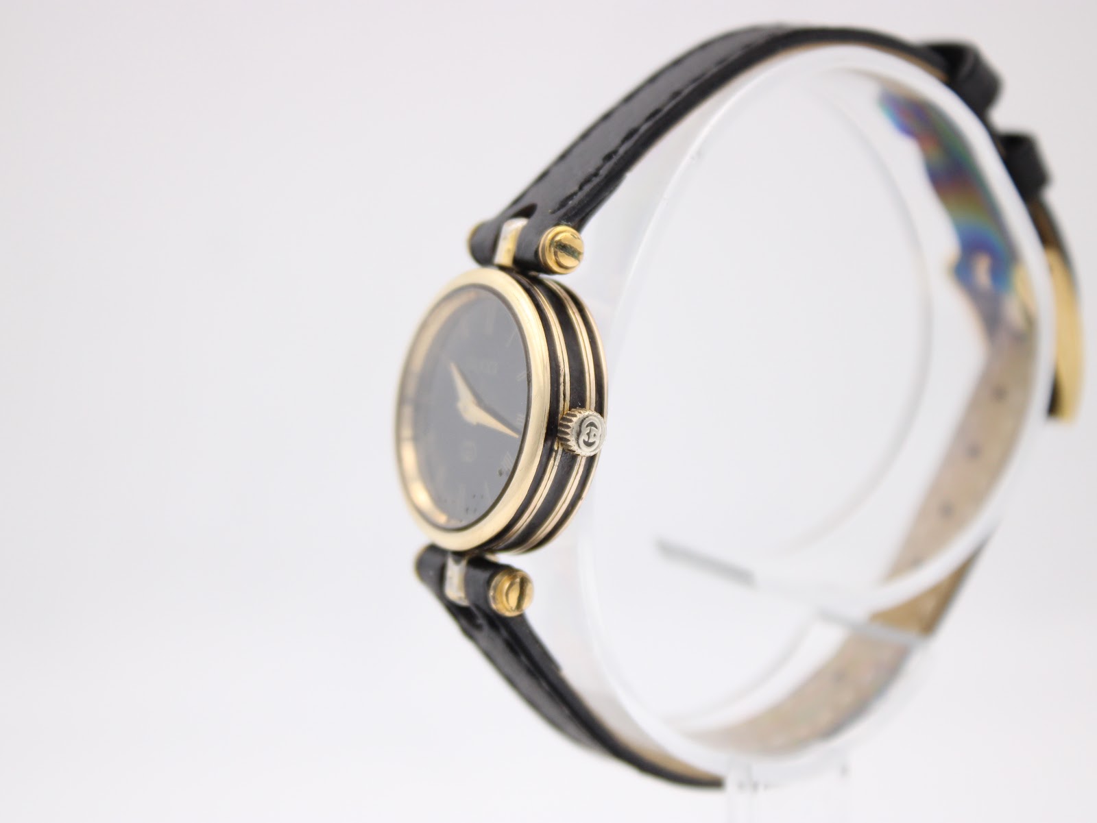 Side view of the Gucci 2000L watch on a stand, highlighting the slim profile and gold-plated case and original crown.