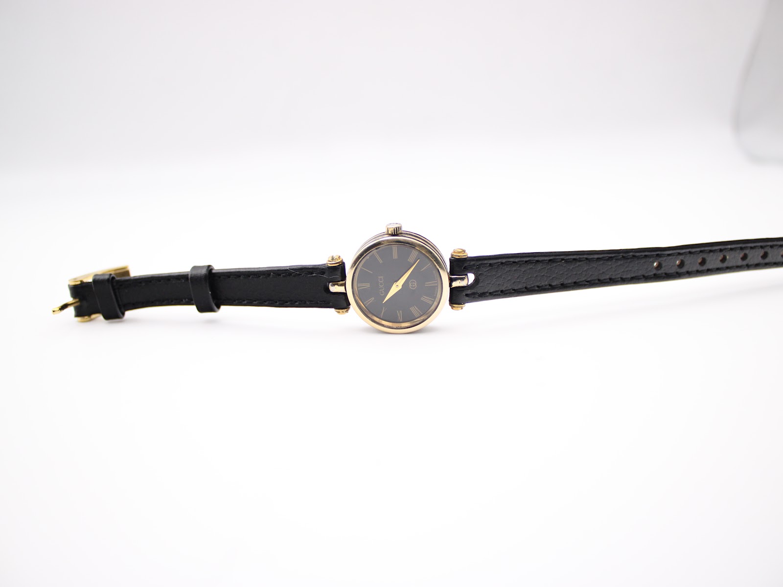 Top-down view of the watch with the black leather strap extended, showing the dial and gold buckle.