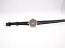 Top-down view of the watch with the black leather strap extended, showing the dial and gold buckle.