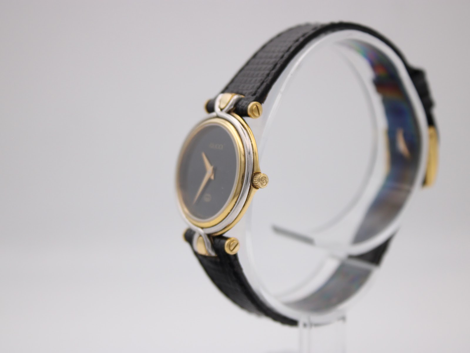 Angled side view of the Gucci 4500L watch showing the two-tone case, gold-tone crown, and black leather strap.