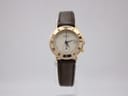 Front view of the Gucci 3800L watch with gold-plated case, cream dial, Roman numerals, and brown leather strap on a display stand.