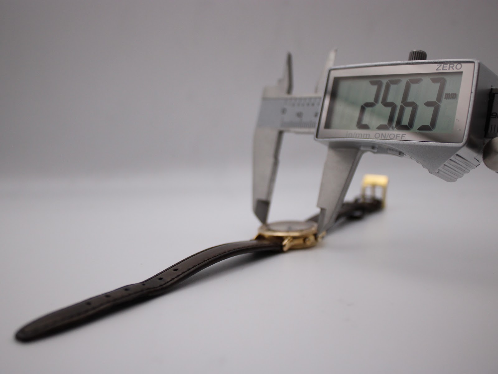 Digital caliper measuring the watch case diameter at precisely 25.63 mm, with the watch and strap extended.