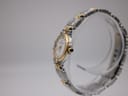 Side profile of the Maurice Lacroix watch on a clear stand, highlighting the gold-tone crown with a blue cabochon.