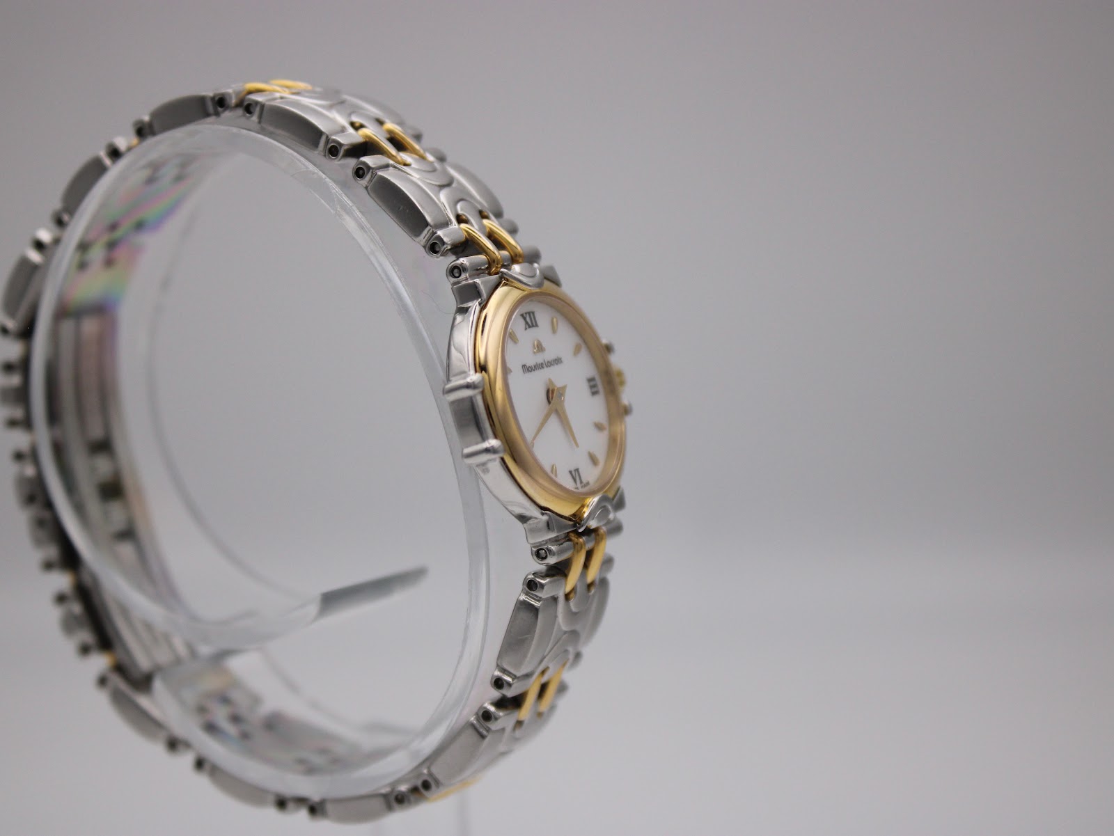 Three-quarter angle of the Maurice Lacroix watch on a clear stand, displaying the bi-colour stainless steel and gold-tone bracelet.