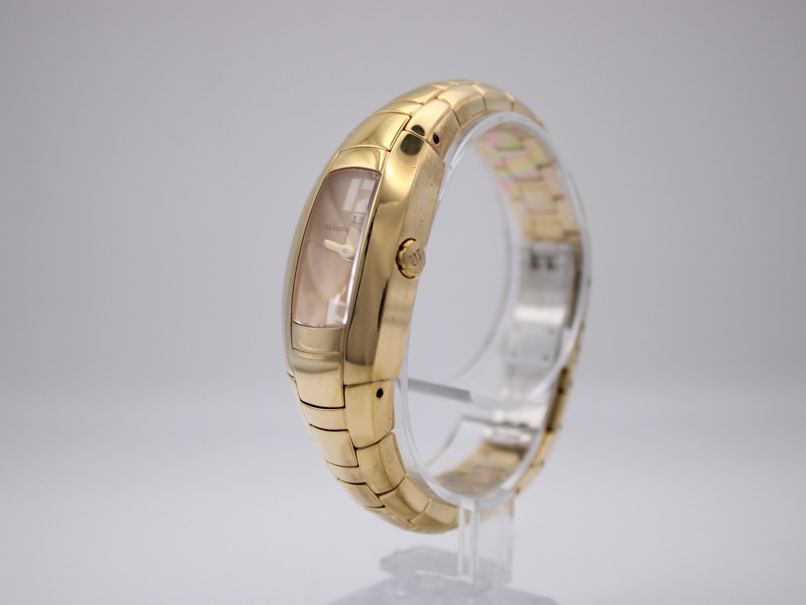 Side view of the Maurice Lacroix watch on a stand, highlighting the curved gold-plated case and integrated bracelet design.