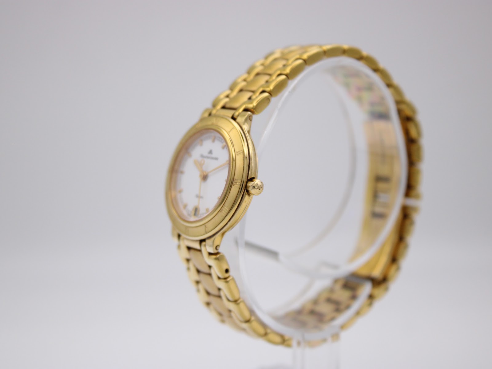 Angled side view of the gold-tone Maurice Lacroix watch and bracelet on a clear stand, showing the curved case profile.