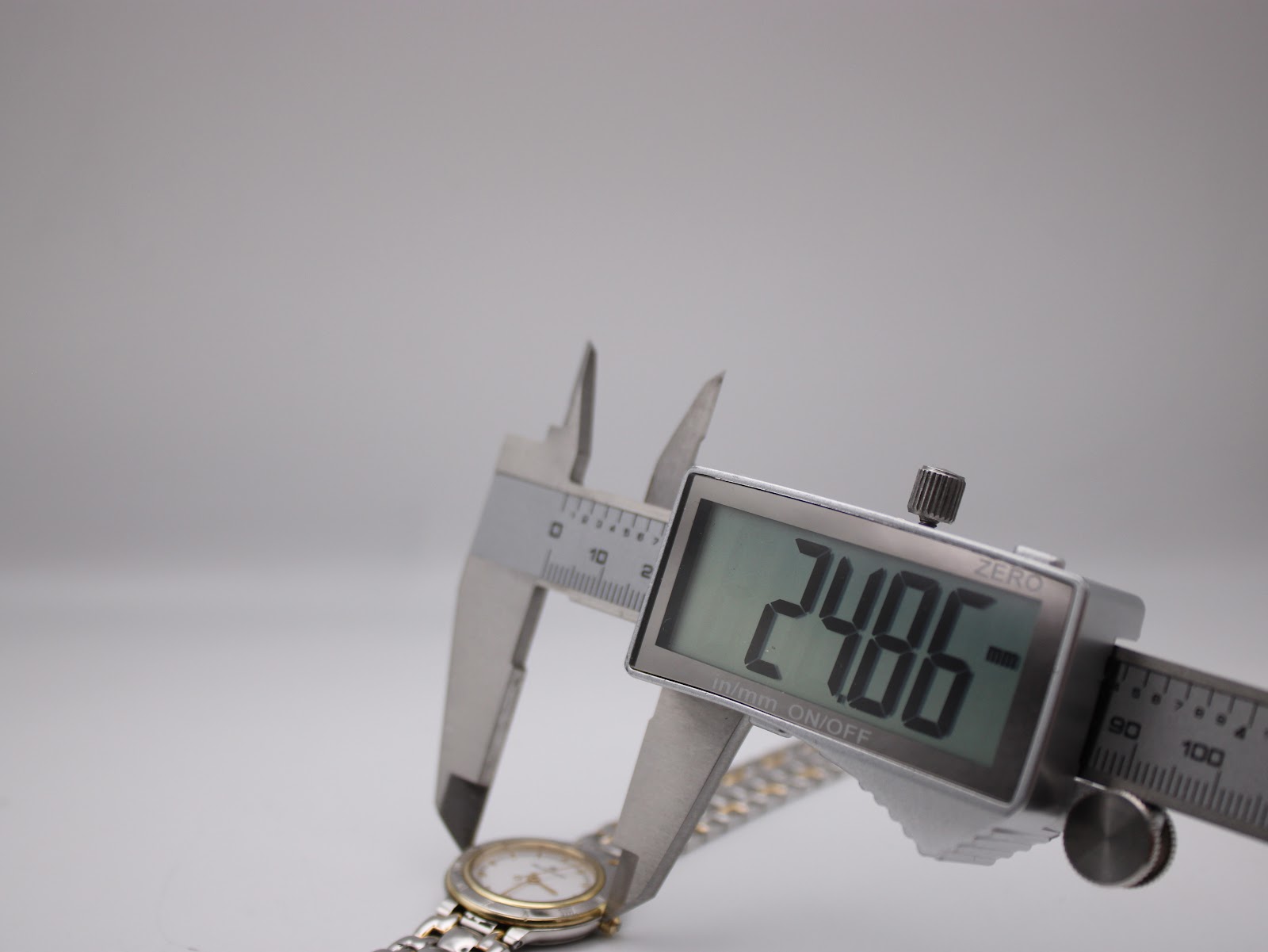 Digital caliper measuring the watch case diameter, displaying 24.86 mm. The watch dial and two-tone bracelet are partially visible.
