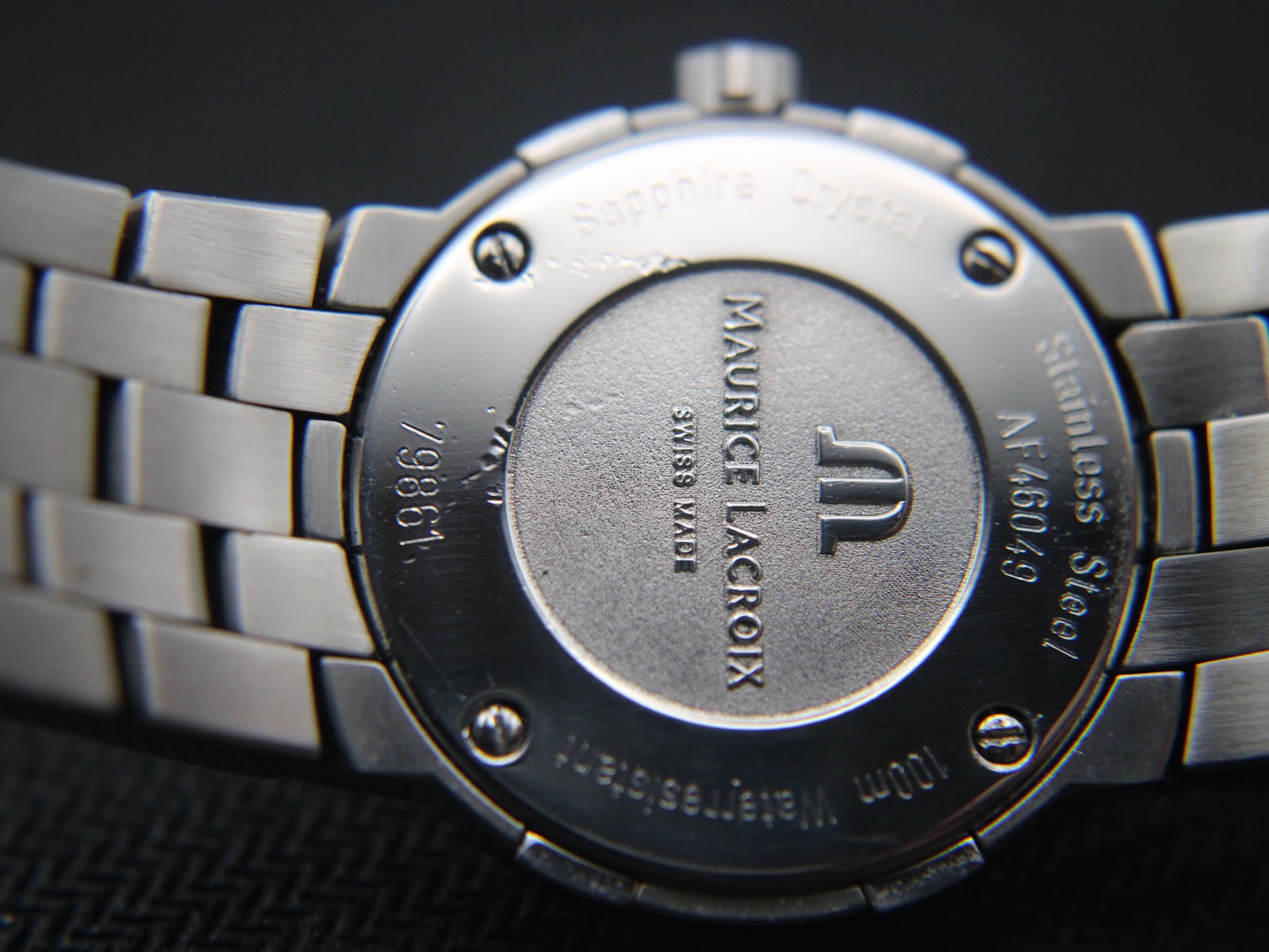 Close-up of the polished stainless steel case back, showing brand, model, serial numbers, sapphire crystal, and 100m water resistance.