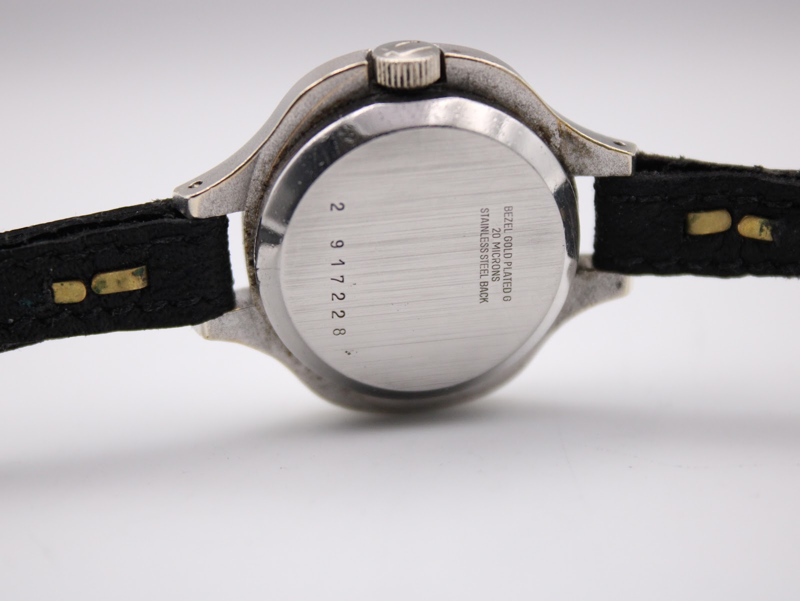 Rear view of the Bulova Accutron watch case back, showing "BEZEL GOLD PLATED G 20 MICRONS STAINLESS STEEL BACK" engraving and serial number.