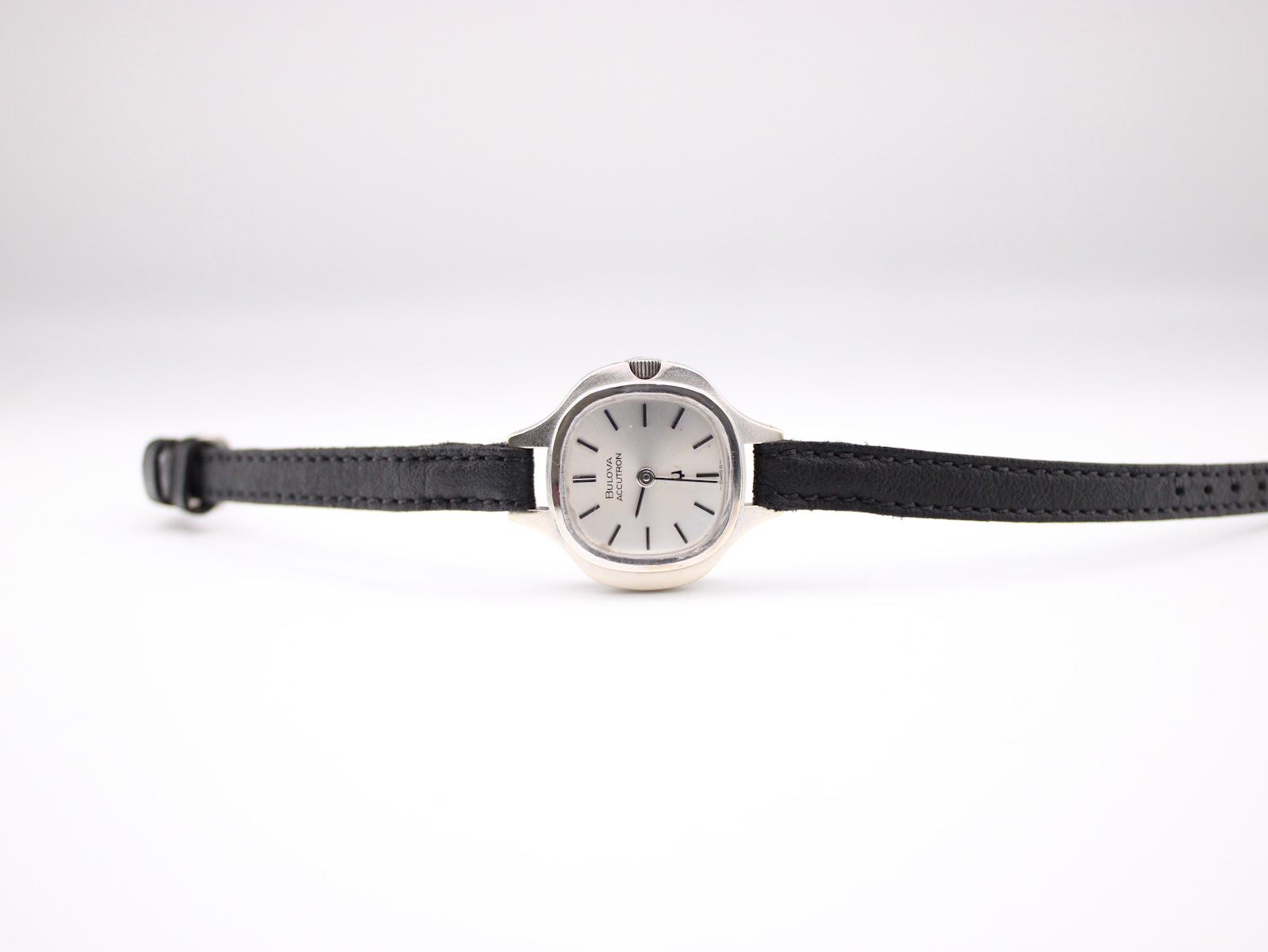 Full front view of the Bulova Accutron watch with black leather strap laid flat.