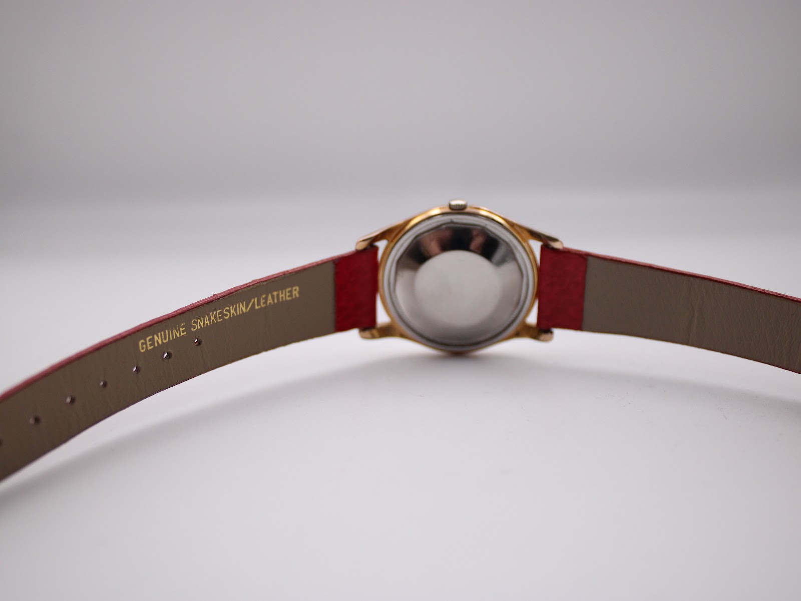 Rear view of the Rone watch showing the stainless steel case back and the red leather strap, with "GENUINE SNAKESKIN/LEATHER" visible on the inside of the strap.