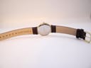 Top-down view of the watch from the back, showing the "GENUINE LEATHER" marking and gold-tone buckle on the new brown strap.