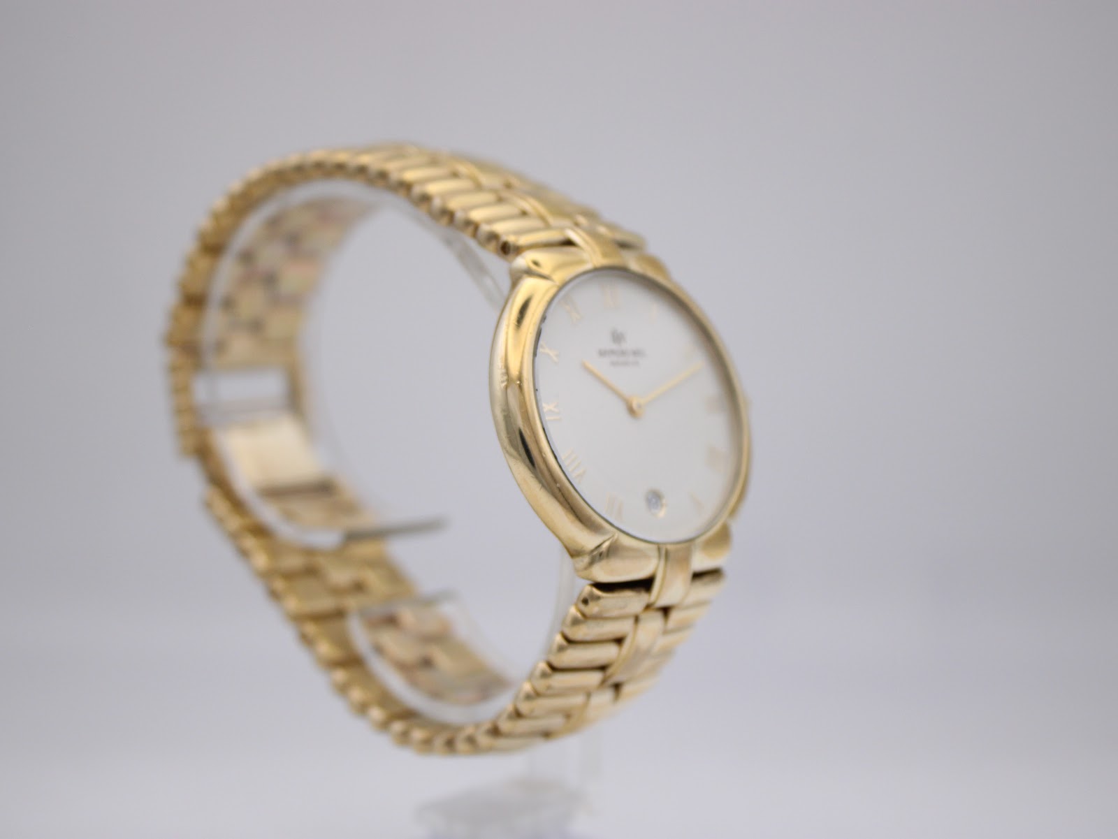 Angled left side view of the Raymond Weil gold plated watch on a stand, highlighting the case profile and bracelet links.