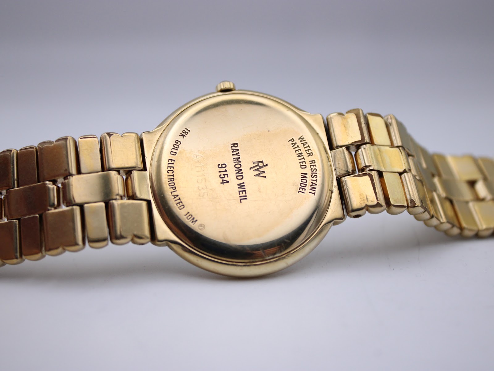 Close-up of the watch's stainless steel case back, showing "Raymond Weil Genève 9154", "18k gold electroplated", and "water resistant 10M" engravings.